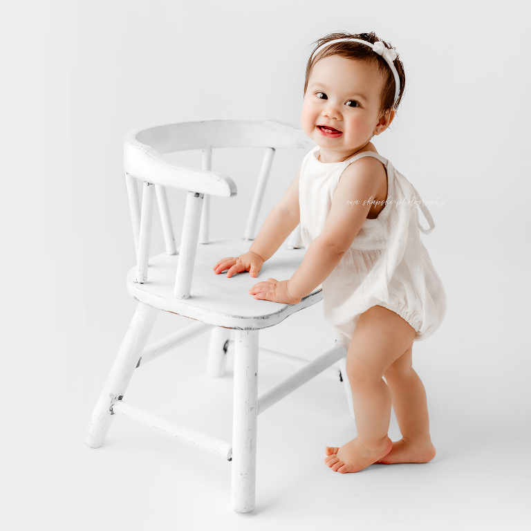 baby standing next to white chair